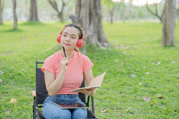 Asian woman sitting listening to music, reading a book, outdoors in nature, evening.