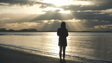 Silhouette of a woman with hat standing on the beach in the morning
