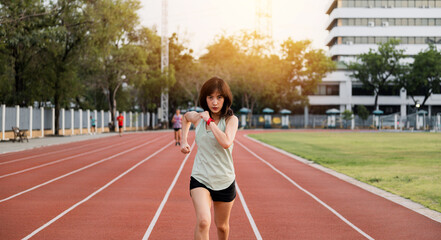 Obraz premium determined southeast Asian woman runner is captured mid stride on track, embodying healthy lifestyle and wellness. scene reflects motivation and challenge of achieving fitness goals