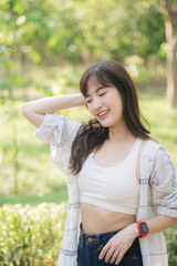 Asian woman enjoying summer outdoors, breathing fresh air with cheerful smile, wearing casual attire in lush green park