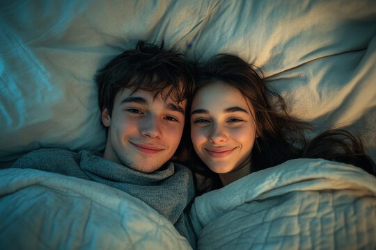Couple cuddling under covers in bed, smiling. - Powered by Adobe