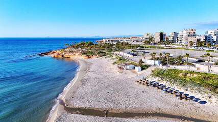 Aerial view Mil Palmeras coastline, showing beachfront houses, promenade, sandy beach and turquoise Mediterranean Sea under clear blue sky, ideal for travel, tourism, real estate. Costa Blanca, Spain