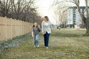 Fototapeta premium A mother and daughter walk hand in hand, filled with laughter and joy as they embrace their outdoor adventure together.