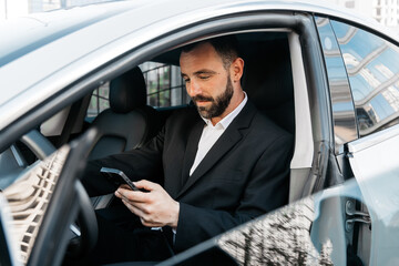Businessman reading a message on his phone in his new modern car. Business concept and modern...