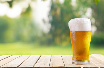 glass of beer on wooden table on green lawn background
