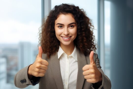 A young businesswoman with curly hair gives a thumbs-up, expressing positivity and success.