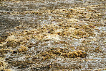 Smudged water flows profusely. River water flowing profusely. Flood waters rushing down river after storm flows through. Turbulent river dam. Water turbulence of river due to dam. Water Nature Texture