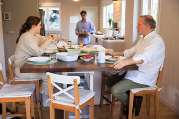 Family Enjoying Lunch Together at Home While adult offspring is bringing More Food