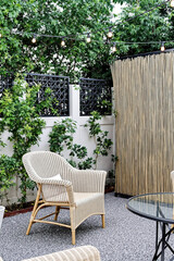 Fototapeta premium beige wicker chair sits on a gravel patio with a bamboo screen and string lights