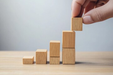 Hand placing wooden block on a stack representing growth or progress.