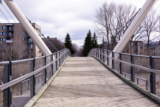 Pedestrian bridge over the Saint-Charles River in the Limoilou sector seen during a cloudy spring morning, with back view of man and dog in the background, Quebec City, Quebec, Canada