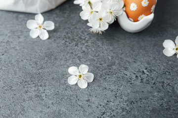 Decorative spring flowers and an orange egg on a textured gray surface