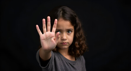 A solemn child holds up a hand in a gesture of refusal or warning, against a black background. Her serious expression conveys a powerful message of strength and awareness for child abuse prevention.