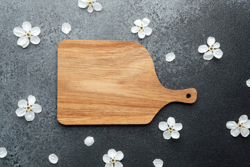 Wooden cutting board surrounded by delicate white flowers on a dark surface