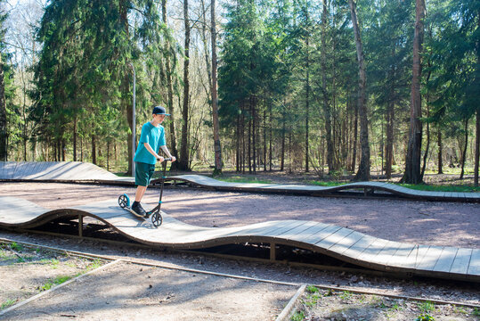A 12 year old boy in a cap and shorts rides a scooter on a pump track in Borovsky Park in Moscow in the spring.