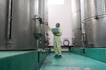 Wine factory, wine production, produces wine. Winemaker inspecting quality the process of fermentation during manufacturing in winery factory and stainless tank. Winemaker working with laptop computer