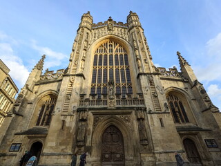 Low angle view of the intricate Gothic facade of Bath Abbey under a blue sky with clouds