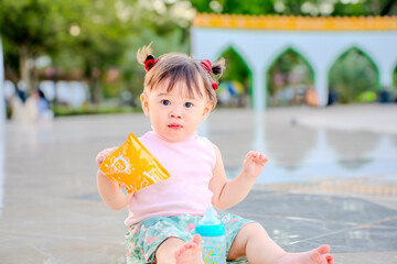 Cute Toddler Girl Sitting Outdoors and Eating Snack at Public Park Near Mosque