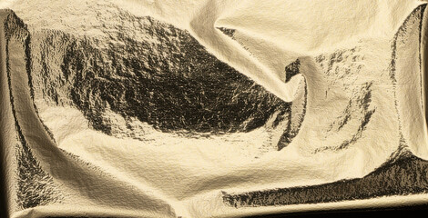 Gold metallic foil texture background. Crumpled, shiny surface with a reflective, polished finish....