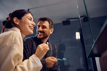 Happy couple having fun while brushing their teeth in bathroom.