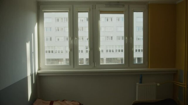 A 4K video showing warm sunlight entering a dormitory room in Wrocław, Poland. The camera captures shadows cast on the walls through large windows with a contrast between yellow and gray tones