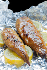Smoked mackerel fillets cooked with sliced lemon on an aluminium background backdrop.