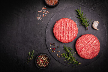 Raw steak burgers patties with ground beef and spices on a cutting board. Dark background, top view.