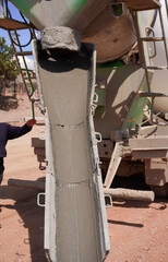 A concrete mixer discharges a steady stream of wet concrete from its chute. The gray mixture flows...
