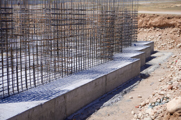 A construction site featuring concrete foundations with exposed steel rebar. Shadows cast by the...