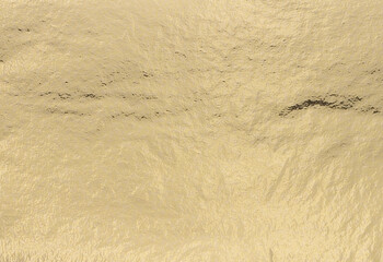 Golden foil texture with metallic, pearlescent shimmer creates a subtle, elegant finish. Soft light highlights the smooth, polished surface, perfect for luxury wrapping, art, and upscale decor..
