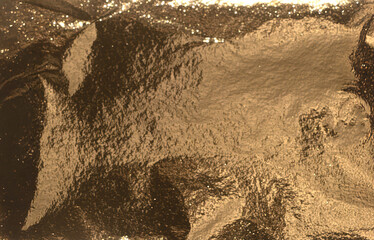 Rich bronze-gold foil surface with heavy shadow contrast and subtle texture. The light reflects in...