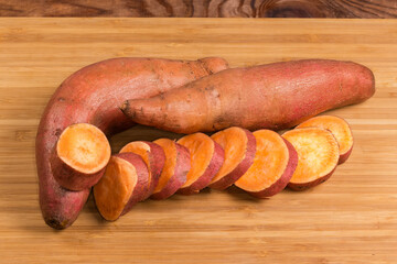Whole and sliced raw sweet potato tubers on cutting board