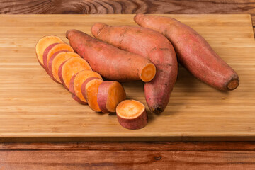 Whole and sliced raw sweet potato tubers on cutting board