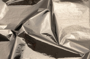 Silver foil with shiny, metallic texture creates a smooth, reflective surface. Crinkled, folded angular design adds modern elegance and high contrast, ideal for minimalistic wrapping, luxury craft,.