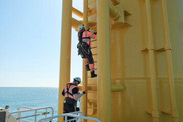Offshore Rigger Technician Climbing Yellow Wind Turbine Monopile Ladder During Wind Farm...