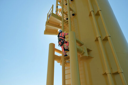 Offshore Rigger Technician Climbing Yellow Wind Turbine Monopile Ladder During Wind Farm Construction Maintenance, GWO Work On Height