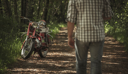 Homem a caminho da moto vintage vermelha na floresta