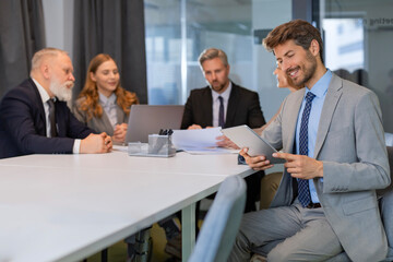 Portrait of adult businessman sitting at his desk in the office and smiling looking at camera