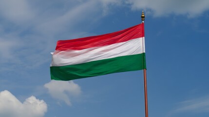 Hungarian national flag waving against blue sky with clouds