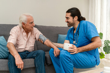 Home male nurse checking senior man's blood pressure at home sitting on sofa