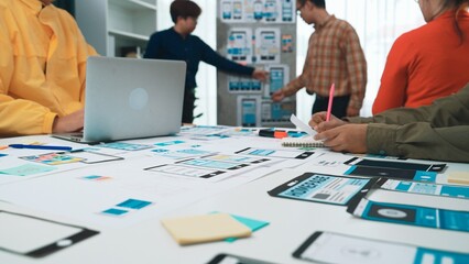 A collaborative team engages in mobile app design, showcasing wireframes, laptops, and colorful...
