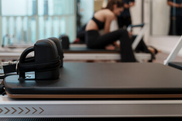 Pilates reformer machine in foreground with blurred woman exercising in background. Modern studio...