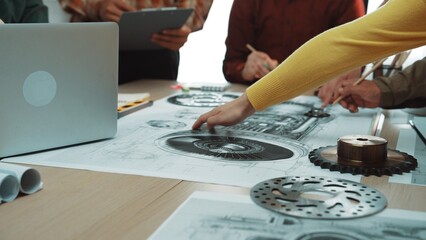Engineers collaborate over detailed technical drawings and blueprints in a modern workspace,...