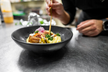 A chef delicately garnishes a bowl of creamy mashed potatoes topped with roasted chicken and herbs. The careful detail showcases culinary expertise in a modern kitchen environment.
