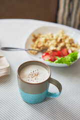 Breakfast table. Cup of coffee and plate with scrambled eggs and vegetables on the table