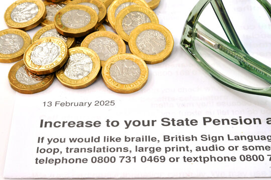Close up view of a letter about an increase the the State Pension in the UK, with one poind coins and a pair of reading glasses. No people.