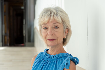 Close-up of a mature woman with a short haircut, dressed in blue, against the background of an architectural corridor.