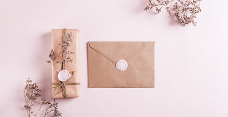 Gift in kraft paper and envelope with wax seals and dried flowers on pink top view web banner