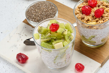 Yogurt and chia seed pudding in a glass, kiwi pieces. White table