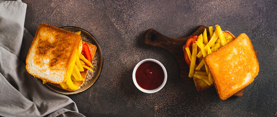 Crispy sandwich with french fries and tomato on a board on a table top view web banner